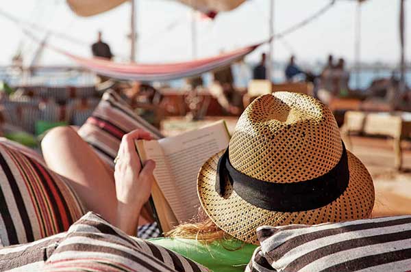 Persona descansado y leyendo en la cubierta con sombrero