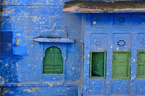 Pared de una casa tradicional en India pintada en azul con ventanas en madera color verde