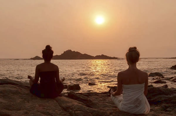 Dos personas meditando al atardecer en SwaSwara con el sol a contraluz
