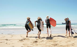 Varias personas jóvenes sobre la plata corren al mar con sus tablas de surf. 